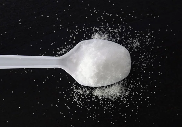 Sugar in spoon on black — Stock Photo, Image