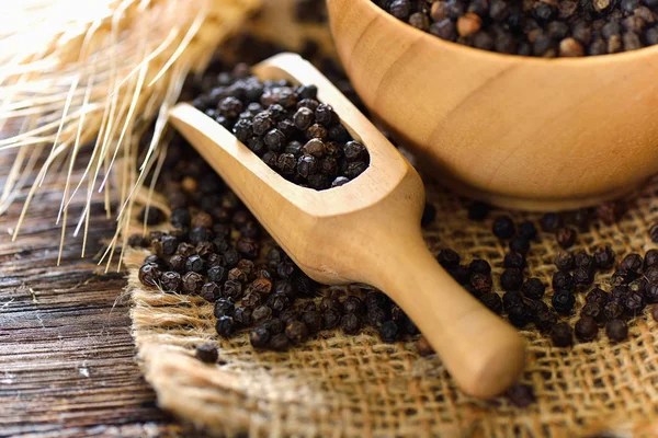 Black pepper seeds in wood scoop on table — Stock Photo, Image