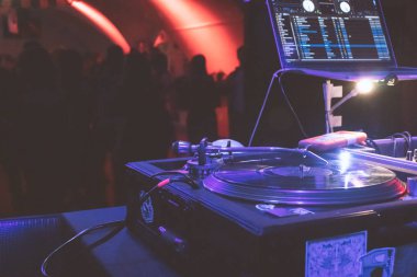 Yakın plan DJ masası, arka planda dans eden insanlar.