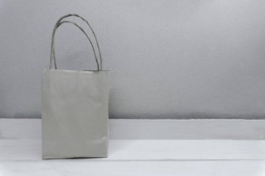 Tahta beyaz masada alışveriş yapmak için sapları olan boş bir kağıt çanta ve beton duvarda kopya alanı var.