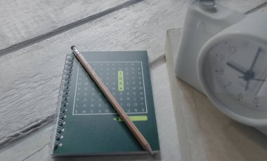 Yeşil kitaplar, kalemler, çalar saat, beyaz ahşap bir masa.