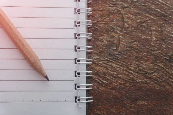 Boş bir defter ve tahta masa üzerinde kurşun kalem. Eğitim kitabı konsepti en üstte