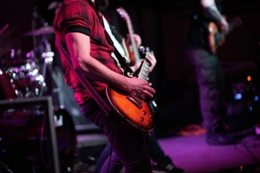 Rock grubu sahnede çalıyor. Gitarist, bas gitar ve bateri. Gitarist çalıyor..