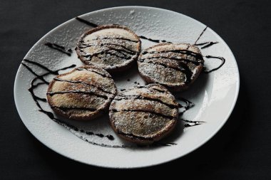 Siyah desenli beyaz bir tabakta servis edilen ev yapımı çikolatalı krepler.