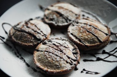 Siyah desenli beyaz bir tabakta servis edilen ev yapımı çikolatalı krepler.