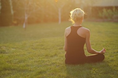 Bahçedeki bir paspasın üzerinde meditasyon pozisyonunda yoga yapan genç bir kadın..
