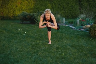 Bahçedeki bir paspasın üzerinde meditasyon pozisyonunda yoga yapan genç bir kadın..