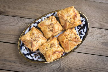 Patates, et ve balkabağı tabakta samosa ve ahşap arka planda geleneksel Özbek süsü, tandırda pişirilmiş. Ulusal Özbek hamur işleri. Düz taban. Üst manzara. Sokak yemeği. Kırsal biçim