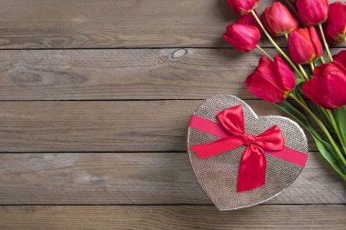 Yakın plan kalp şeklinde hediye paketi ve ahşap masa üstünde güller.