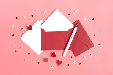 Sevdiğine mesaj göndermek için beyaz bir sayfa, kırmızı zarf, pırıltı, pembe arka planda kalem. Sevgililer Günü konseptin kutlu olsun. Modayı takip et.