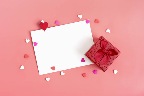 A white sheet of paper for a message to a loved one, a red envelope, a gift box and candy in the shape of hearts on a pink background. Happy valentines day concept Flat lay Mock up Place for text