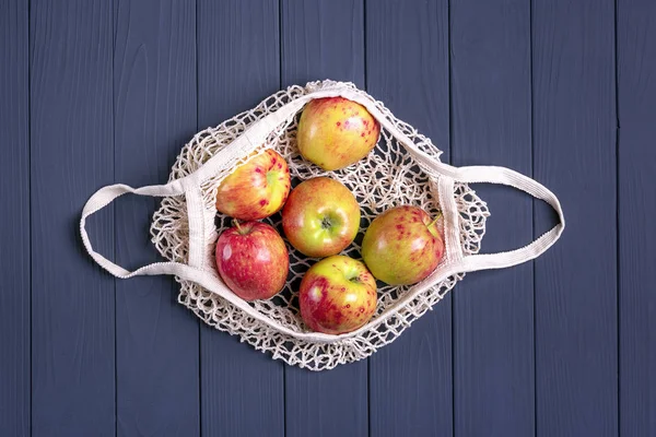 Sonbahar hasadı. Koyu gri ahşap arka planda sulu elmalı, çevre dostu ağ torbası. Düz yerde, üst tarafta. Sıfır atık, plastiksiz konsept. Sağlıklı beslenme ve detoks kavramı
