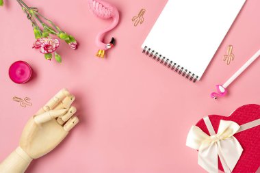 Kadın eşyaları - defter, flamingo, kalem, karanfil çiçekleri, ahşap el, mum, ataç, kaktüs, pembe zemin üzerinde hediye kutusu kalbi