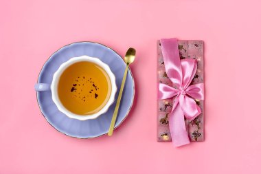 Kuru üzümlü pembe çikolata ve leylak tabağında fındık, bir fincan siyah çay, pembe arka planda altın kaşık Tatlı Zamanı konsepti.