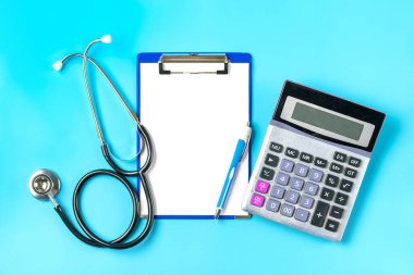 Foneendoskop, hesap makinesi, beyaz kağıtlı tablet, mavi arkaplan üzerine kalem, teşhis, sağlık, hayat, sağlık sigortası konsepti Üst görünüm düzgörünüm