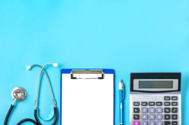 Foneendoskop, hesap makinesi, beyaz kağıtlı tablet, mavi arkaplan üzerine kalem, teşhis, sağlık, hayat, sağlık sigortası konsepti Üst görünüm düzgörünüm