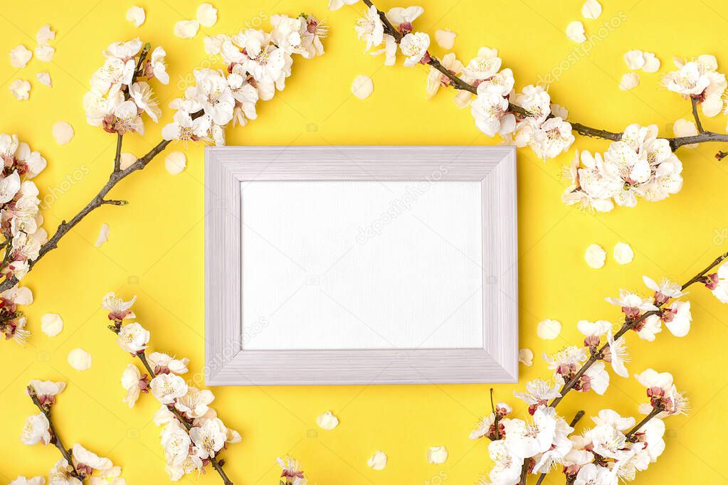 photo frame and sprigs of apricot tree with white flowers on yellow background. Place for text. The concept of spring came, happy easter, mother's day. Top view. Flat lay. Copy space Holiday card.