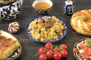 Ulusal Özbek pilavı et, domates salatası, salatalık, geleneksel desenli soğan, kişniş, kiraz domates, sarımsaklı tortilla - koyu ahşap masa üzerine yapıştırılır.