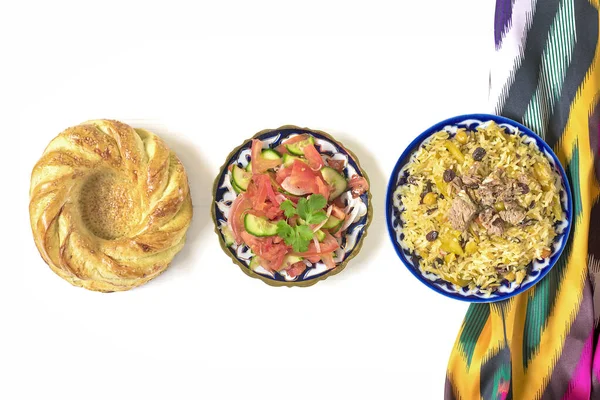 Ulusal Özbek pilavı et, domates salatası, salatalık, geleneksel desenli soğan, kişniş, kiraz domatesleri, sarımsak, ekmek tortilla - beyaz ahşap masa manzaralı.