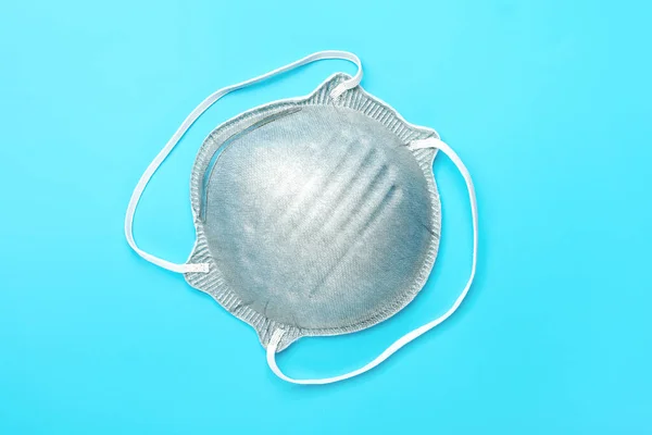 Protective gray medical mask isolated on blue background. Face mask protection against pollution, virus, flu and coronavirus COVID - 19. Health care and surgical concept. Flat lay Top view