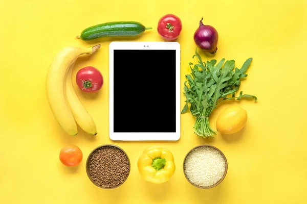 farklı sağlıklı yiyecekler - karabuğday, pirinç, sarı dolmalık biber, domates, muz, marul, yeşil, salatalık, soğan, sarı arka planda siyah ekranlı tablet düz görünüm düz çizgi üzerinde alışveriş