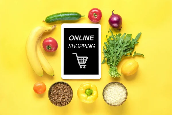 farklı sağlıklı yiyecekler - karabuğday, pirinç, sarı dolmalık biber, domates, muz, marul, yeşil, salatalık, soğan, sarı arka planda siyah ekranlı tablet düz görünüm düz çizgi üzerinde alışveriş