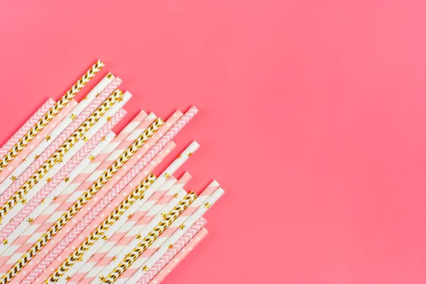 Drinking paper straws for party with golden, white, pink stripes on pink pastel background with copy space. Top view of colorful paper disposable eco - friendly straws for summer cocktails. Flat lay.