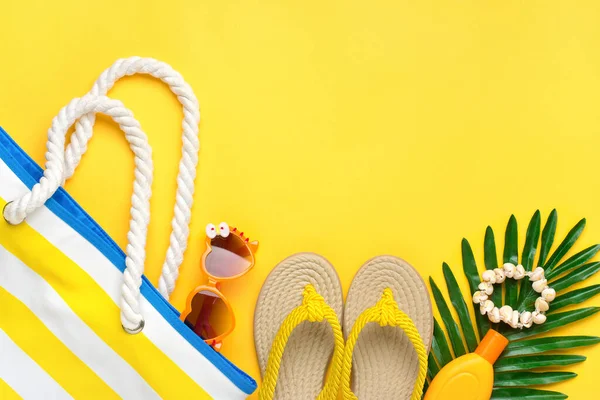 Swimming accessories - trendy beach bag with stripes, sunblock, heart - shaped glasses, palm leaf, flip flop, shells on yellow background Flat lay Top view Summer, travel, vacation concept — Stock Photo, Image