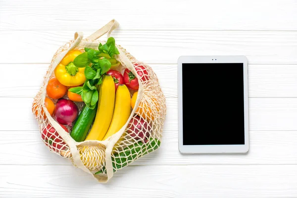 farklı sağlıklı yiyecekler - sarı dolma biber, domates, muz, marul, yeşil, salatalık, soğan, beyaz ahşap arka planda siyah dokunmatik ekranlı ağ tablet