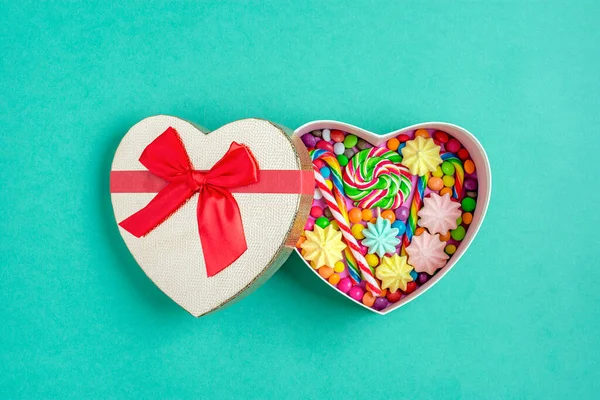 Mezclar dulces de chocolate de colores se encuentran en forma de caja de regalo de corazón sobre fondo colorido plano laico vista superior —  Fotos de Stock