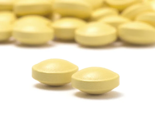 Heap de comprimidos amarelos isolados em um fundo branco — Fotografia de Stock