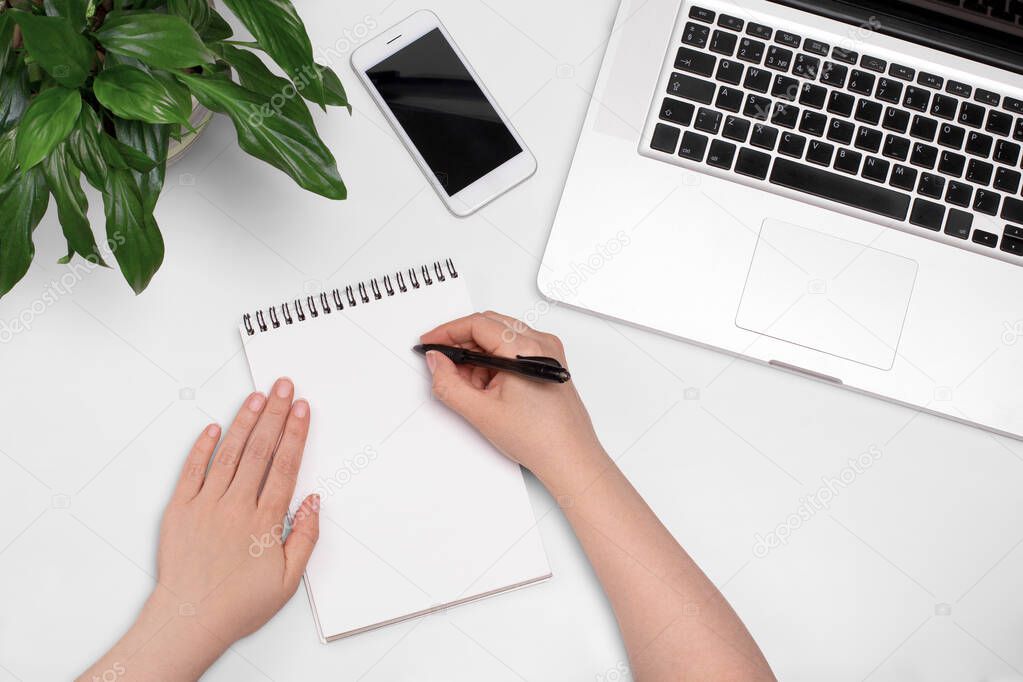 Female hands making notes in notebook. Top view of woman hands, smartphone and laptop. Education, business concept, flat lay.