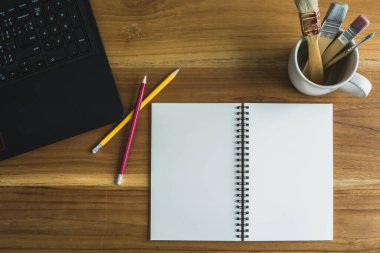 Spiral defter, kalemler, boya fırçaları, ahşap masadaki labirent, metin için boş alan.