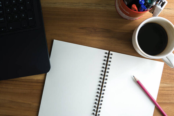 Open spiral notebook, pencil, coffee cup, labtop on wooden table, empty space for your text.