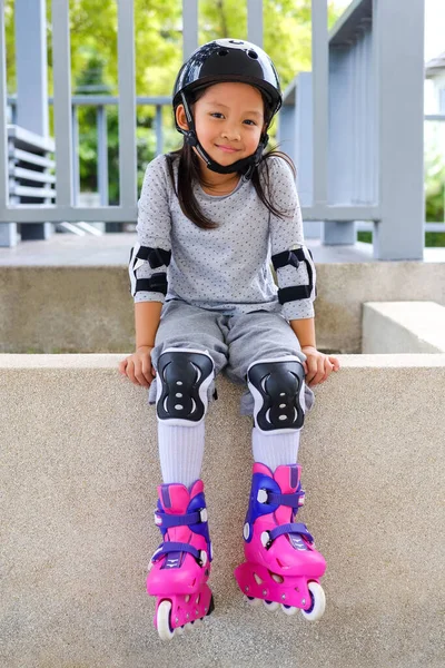 かわいいです笑顔アジアの子供女の子でローラースケートと保護具で公園に座って — ストック写真