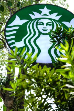 Bangkok, Tayland - 3 Ekim 2018 Ön planda ağaç dalları olan Starbuck Kafe tabelası.