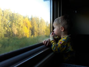 Sarışın, sevimli, üç yaşında bir çocuk trene biniyor.