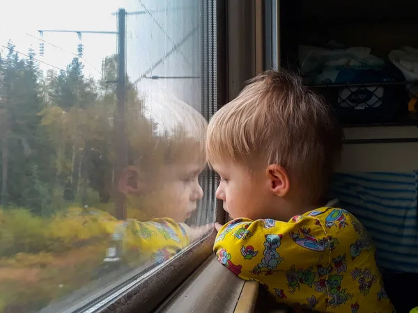 Яркий, милый трехлетний мальчик, едущий на поезде, смотрит в окно, за которым проносится скучный пейзаж . — стоковое фото