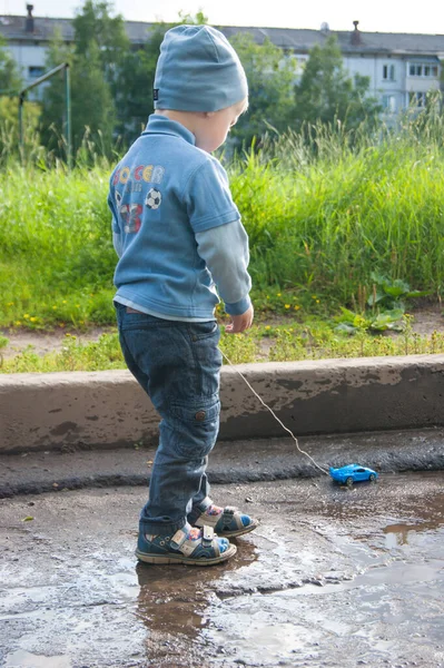 Трехлетний белый парень в синей шляпе, джинсах и сандалиях играет в прохладный летний день с устаревшей машиной дистанционного управления — стоковое фото