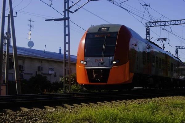 O trem vermelho-cinza varre a cidade resort, o céu é refletido nas janelas. No edifício eu vendo um sinal - uma tradução do russo . — Fotografia de Stock