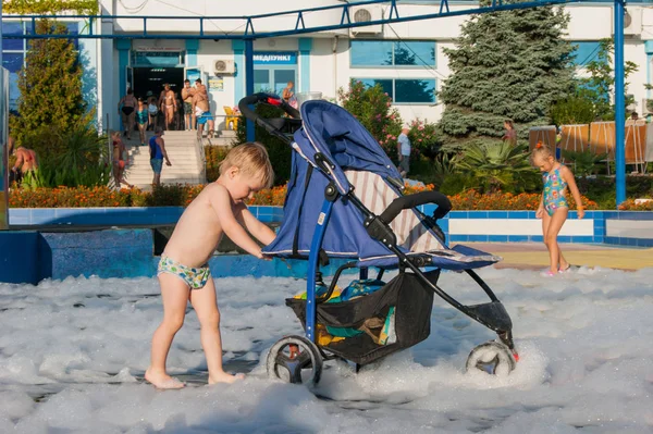 Malý blonďatý chlapec jezdí na kočárku na pěně po pěnové party před hotelem. — Stock fotografie