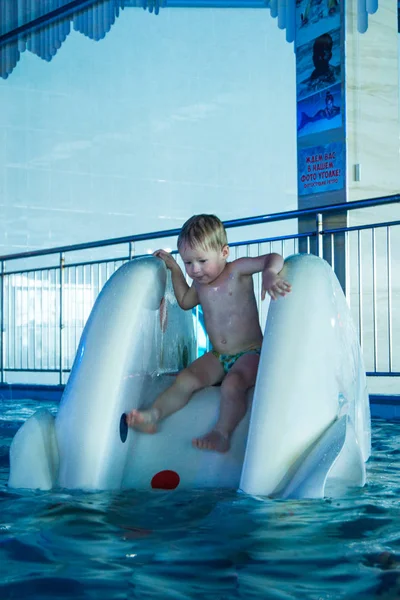 Маленький блондин скачет с холма в крытый бассейн аквапарка — стоковое фото
