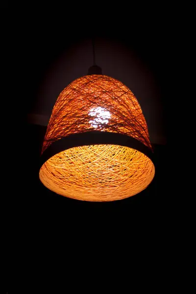 Un paralume retrò arancio intrecciato con una lampadina in stile legno su sfondo scuro. Dettaglio dell'interno. Luce. Foto concettuale verticale — Foto Stock