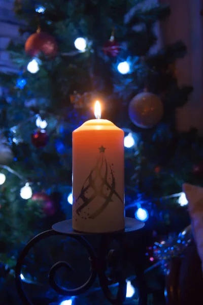 A large candle burns against the background of a garland with shining lights. Vertical photo, defocus. Mystic esoteric romance divination mood christening Christmas carol setcers. — Stock Photo, Image