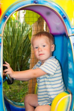 Üç yaşında küçük, sarışın bir çocuk, sırtı izleyiciye dönük bir şekilde Riviera eğlence parkında bir çocuk roketine biniyor. Dinlenme, tropik bölgeler, dinlenme, hareketlilik. Dikey fotoğraf