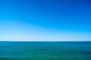 Sakin deniz ve mavi gökyüzü, yatay fotoğraf. Ufuk çizgisi fotoğrafı ikiye böler.