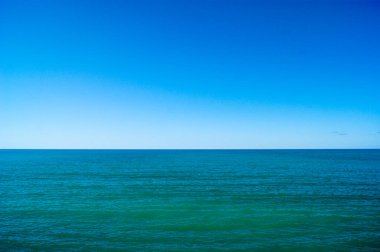 Sakin deniz ve mavi gökyüzü, yatay fotoğraf. Ufuk çizgisi fotoğrafı ikiye böler.