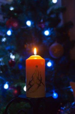 Parlak ışıkları olan bir çelengin arka planında büyük bir mum yanar. Dikey fotoğraf, odak kaybı. Mistik esrarengiz romantizm kehaneti Noel şarkıcılarını vaftiz etme ruh hali.