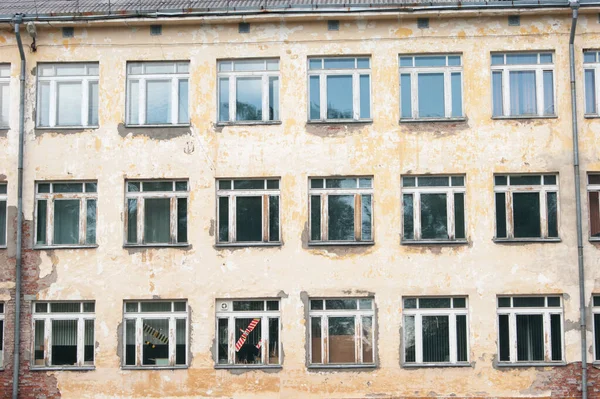 Decorative background - wall, windows. The photo shows the orange wall of the old school and many windows, in one of which a toy airplane is visible in red. Paint and stucco peeled off the walls of the building in parts. I really need a repair. Pover