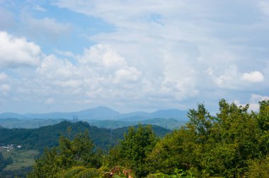 Kafkasya 'nın dağlarında öğle vakti - yatay fotoğraf - dağ manzarası. Beyaz bulutlu mavi gökyüzü ve yeşil ağaçlarla kaplı güzel sıradağlar..
